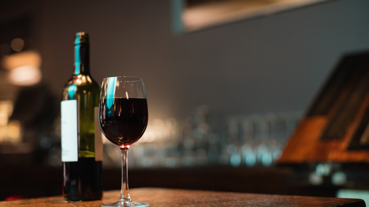 Gros plan sur un verre de vin avec une bouteille à côté, le tout posé sur un bar. 
